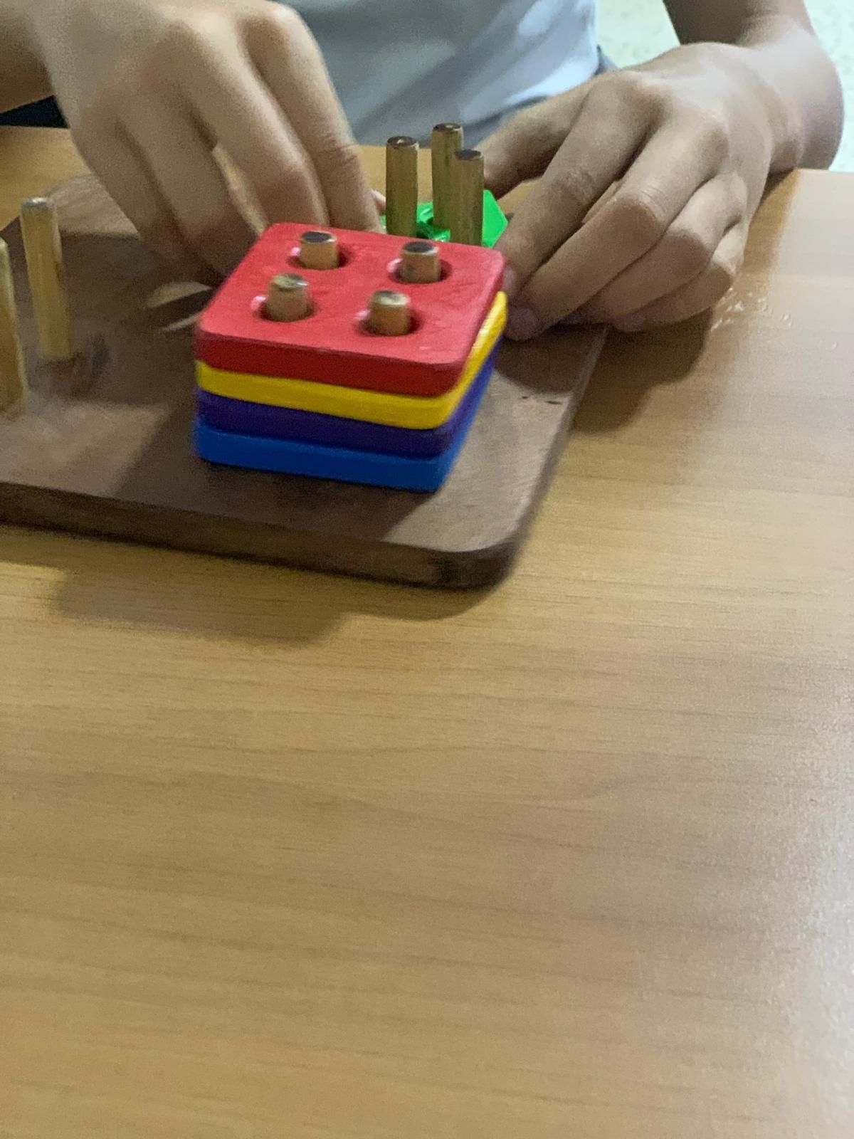 Persona jugando con un tablero de madera y bloques de colores apilables sobre una mesa.
