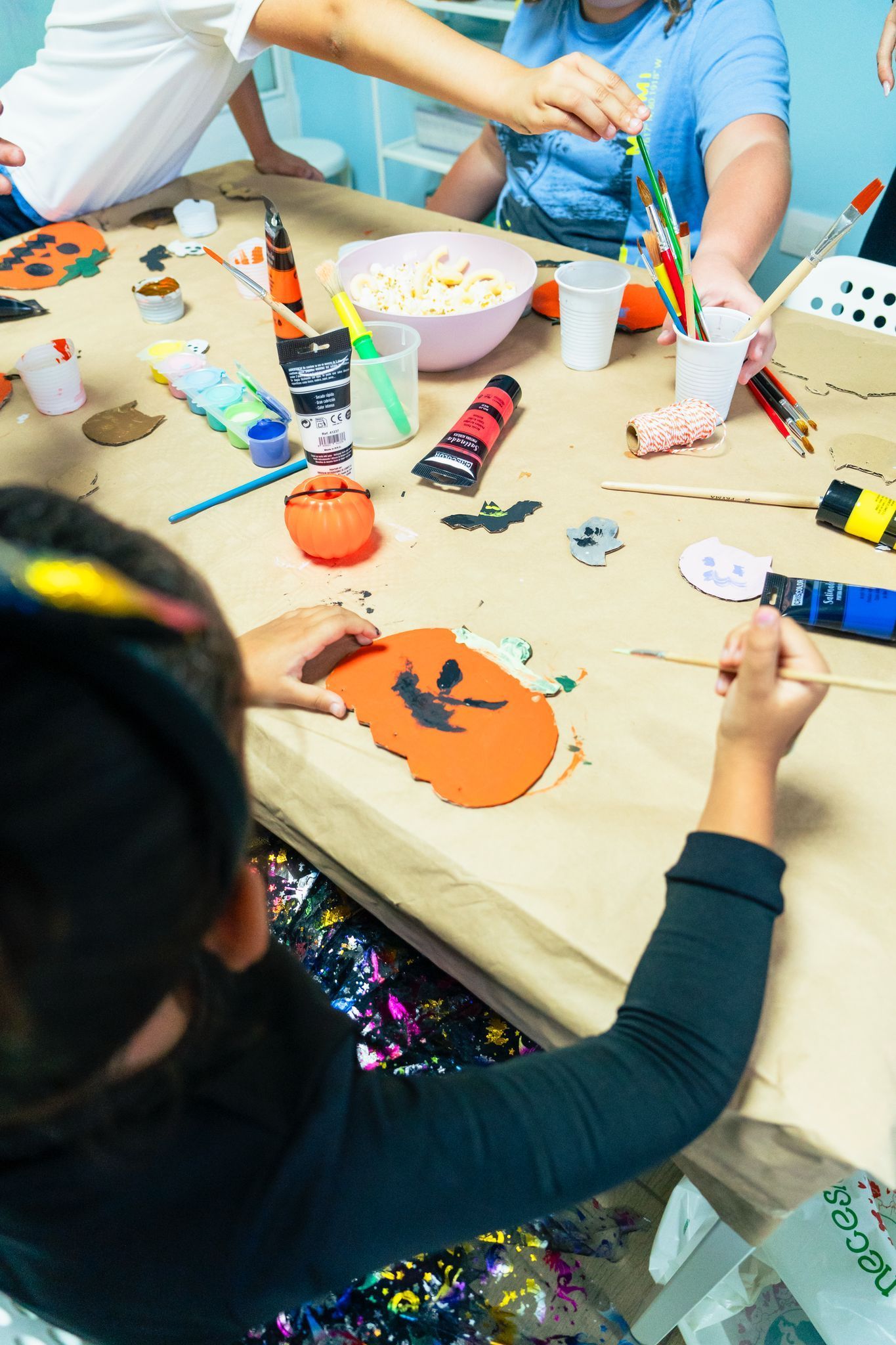 Un grupo de niños está sentado en una mesa pintando calabazas.