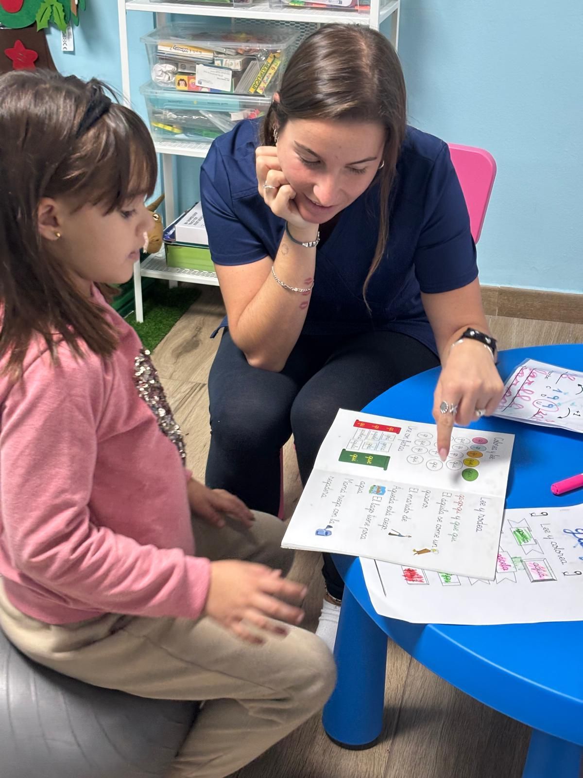 Una mujer señala una hoja de trabajo, ayudando a una niña en una clase.