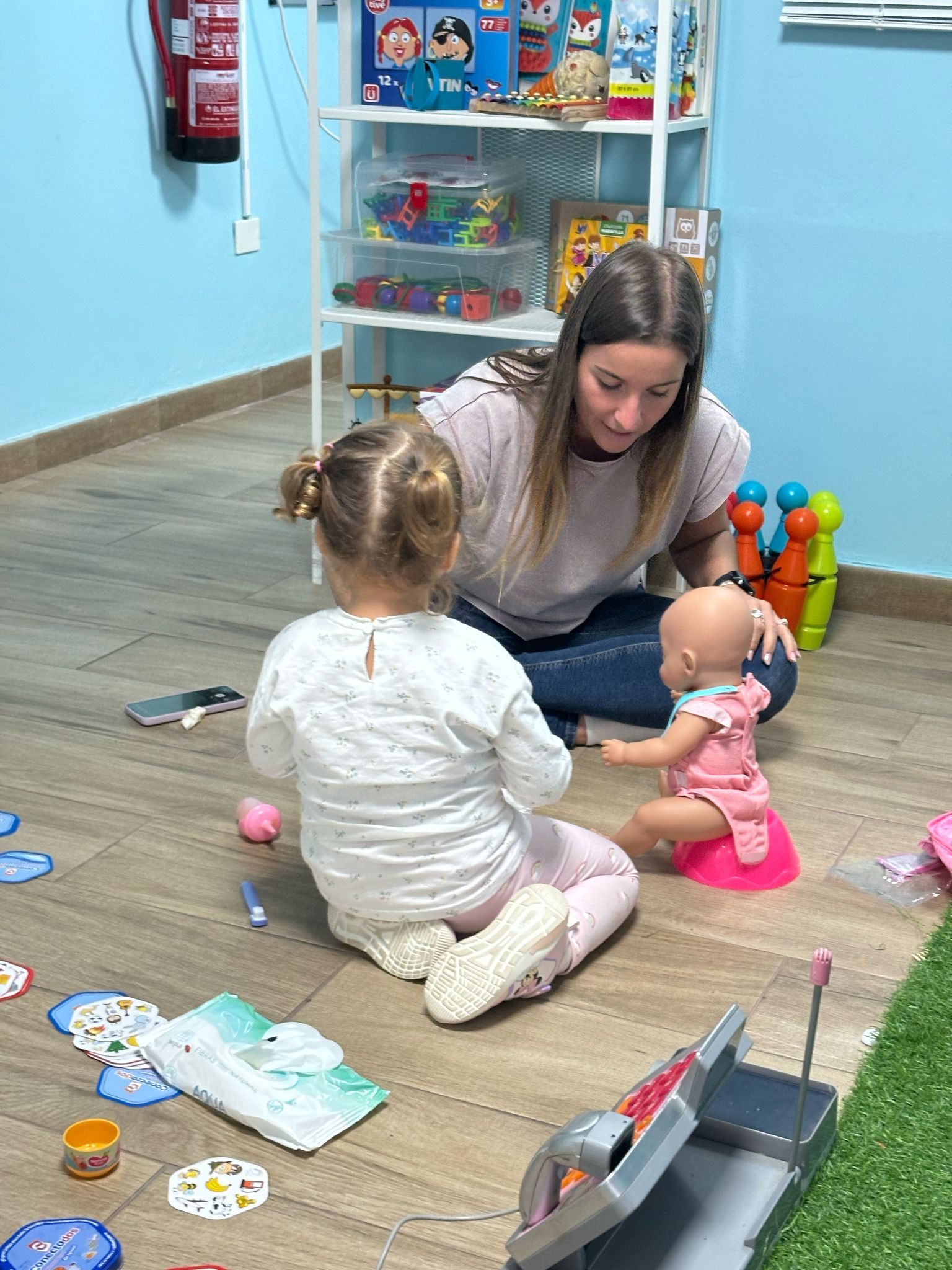 Mujer y niño pequeño jugando con una muñeca en el suelo de una sala de juegos.