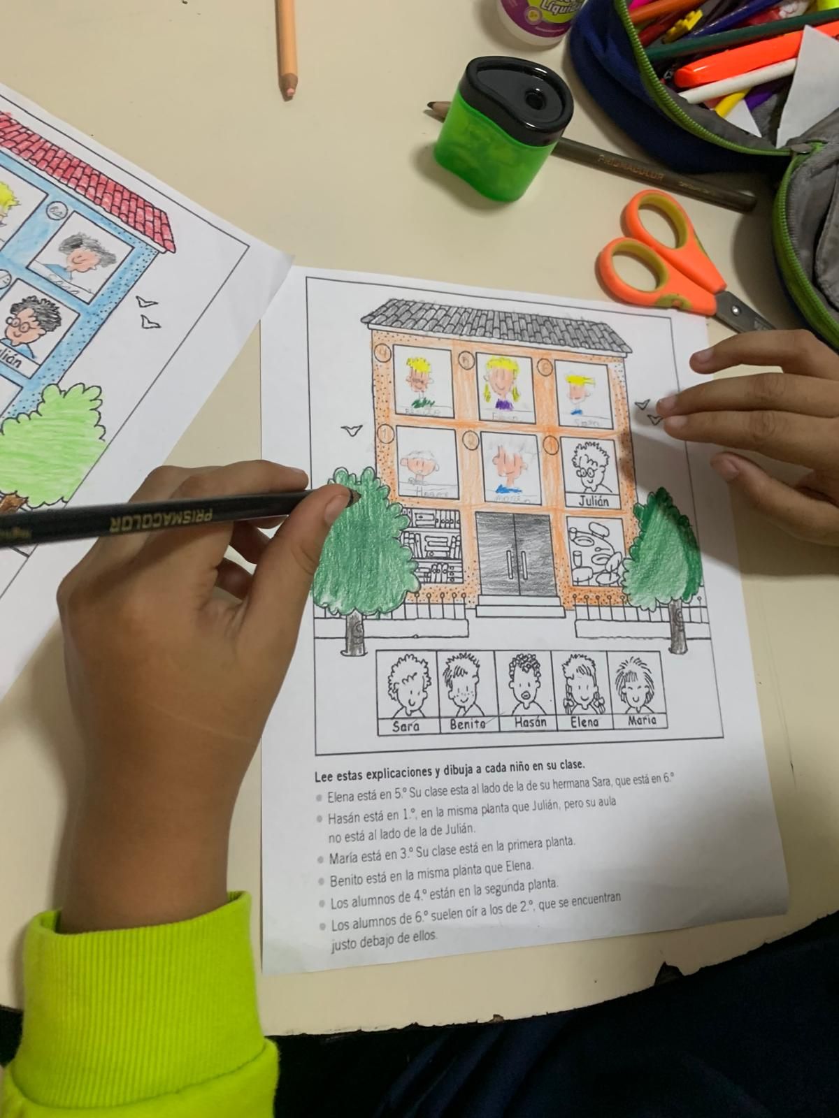Niño coloreando un diagrama de una casa con figuras, texto en portugués y útiles escolares.