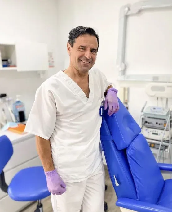 Un hombre con una bata blanca está de pie junto a un sillón dental azul.