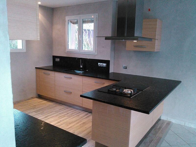 Cuisine moderne avec armoires en bois, comptoirs noirs et îlot avec cuisinière.