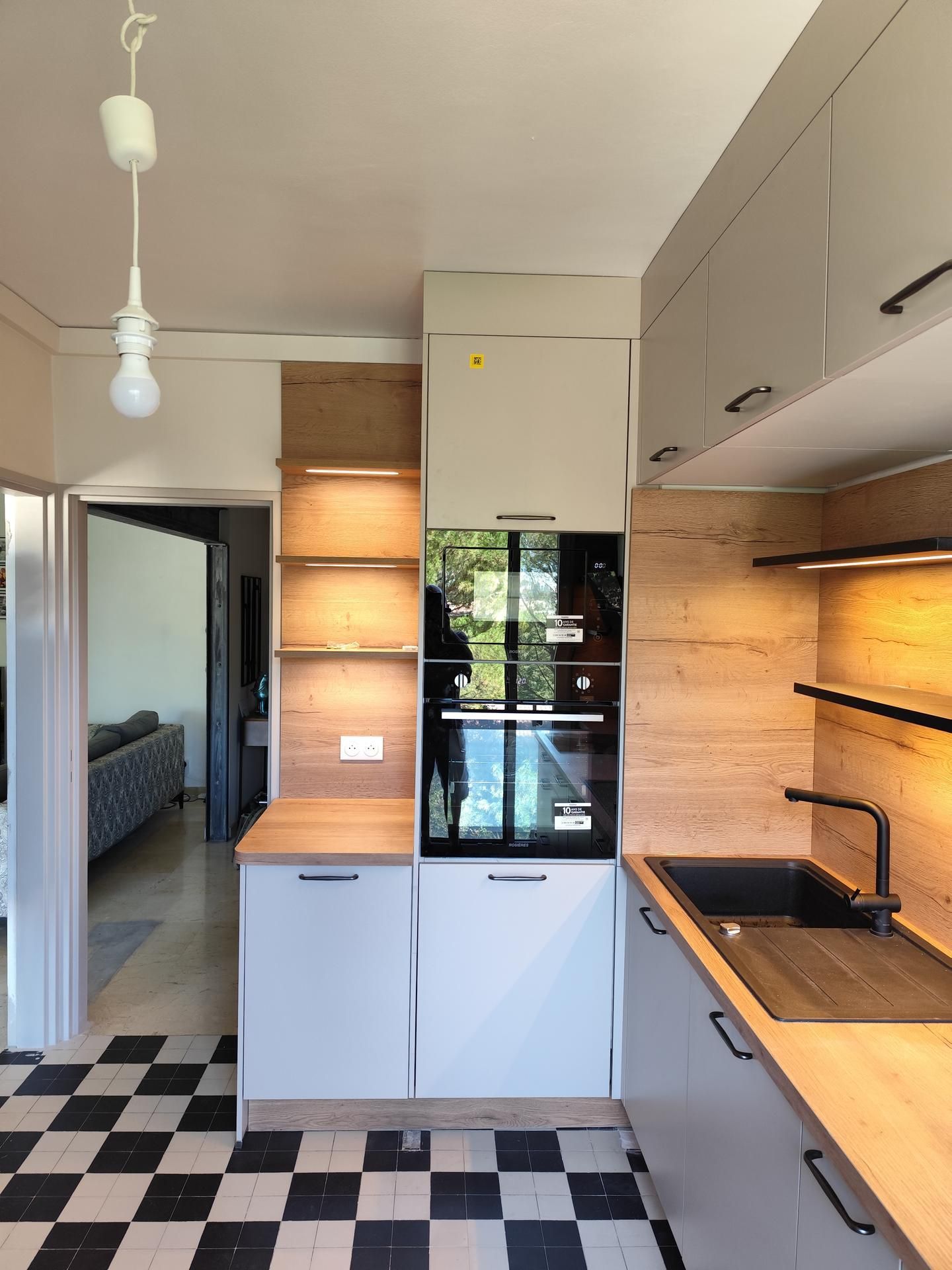 Cuisine moderne avec armoires grises, accents en bois et sol à carreaux noirs et blancs.