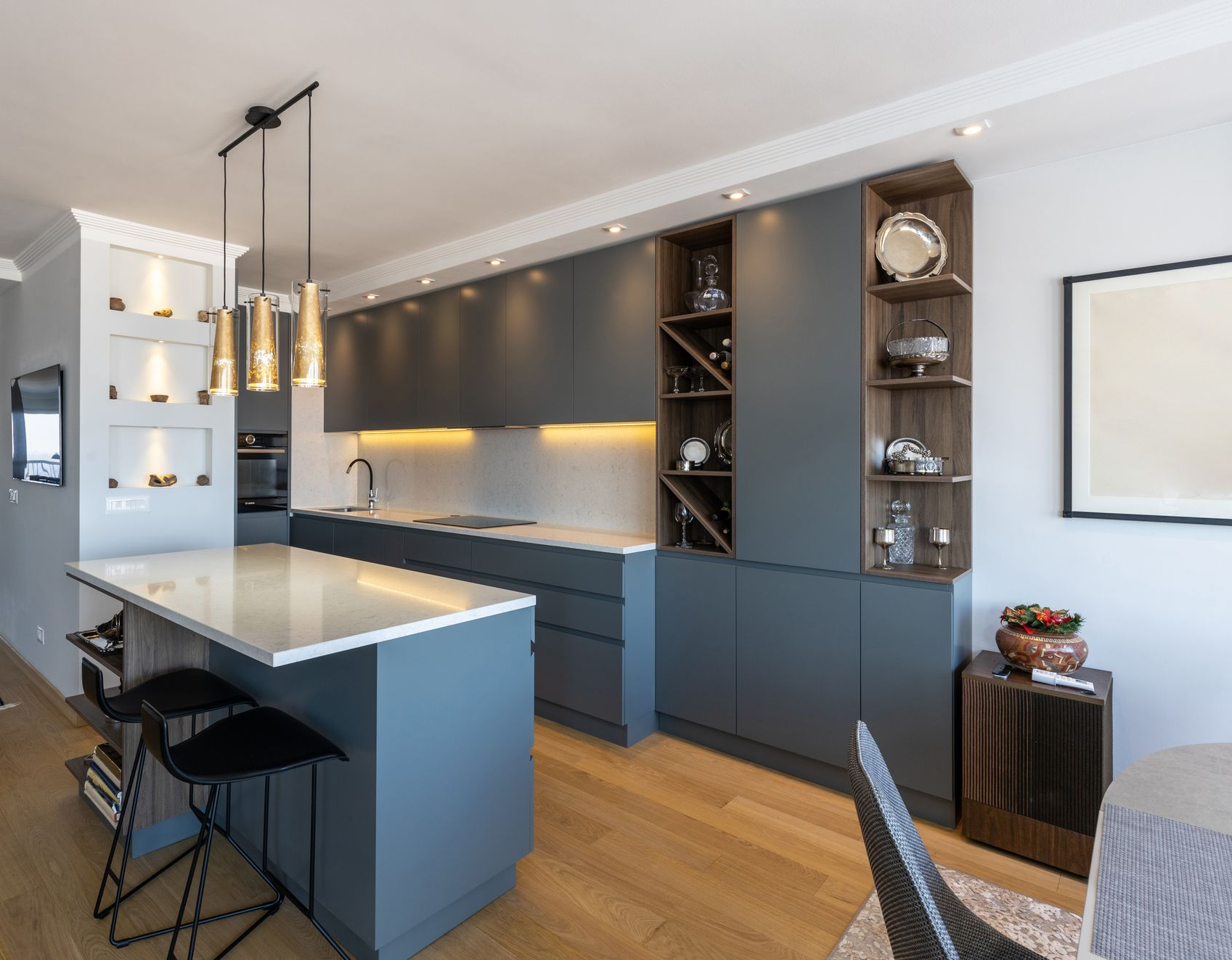 Cuisine moderne avec armoires grises, îlot avec tabourets, étagères en bois et casier à vin.