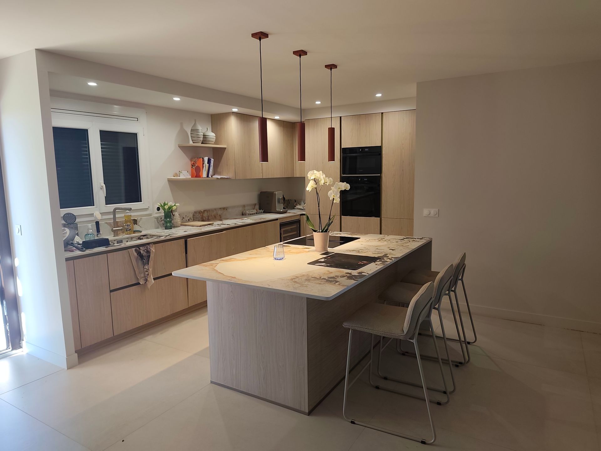 Cuisine moderne avec armoires en bois clair, un îlot et des luminaires suspendus.