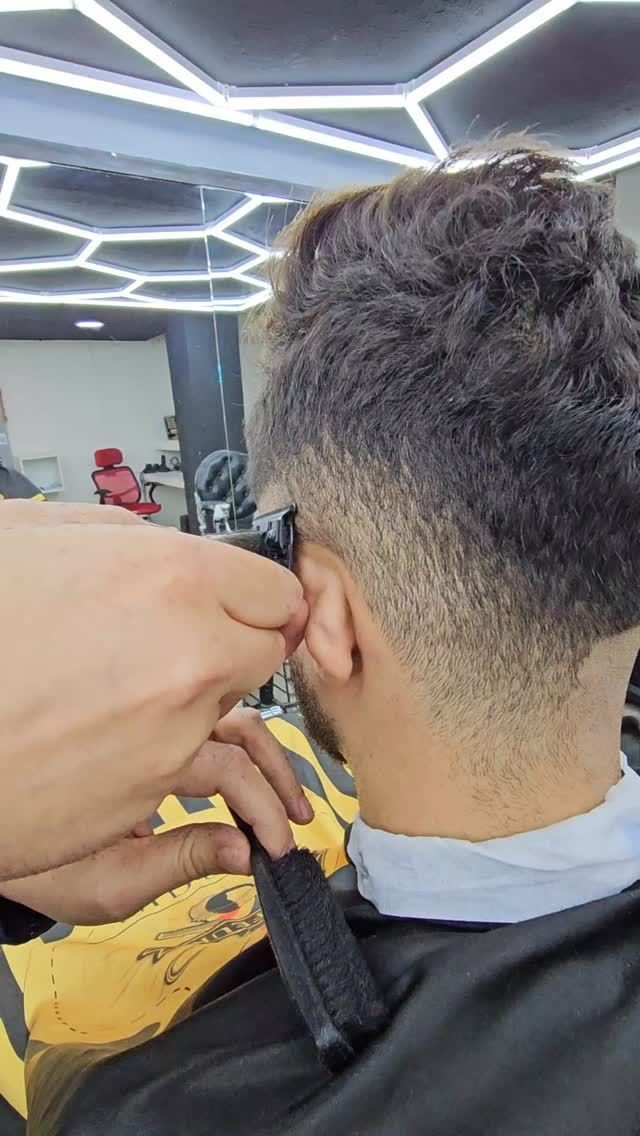 Barbero cortando el pelo, decolorando los lados de la cabeza de una persona con una máquina en un salón.