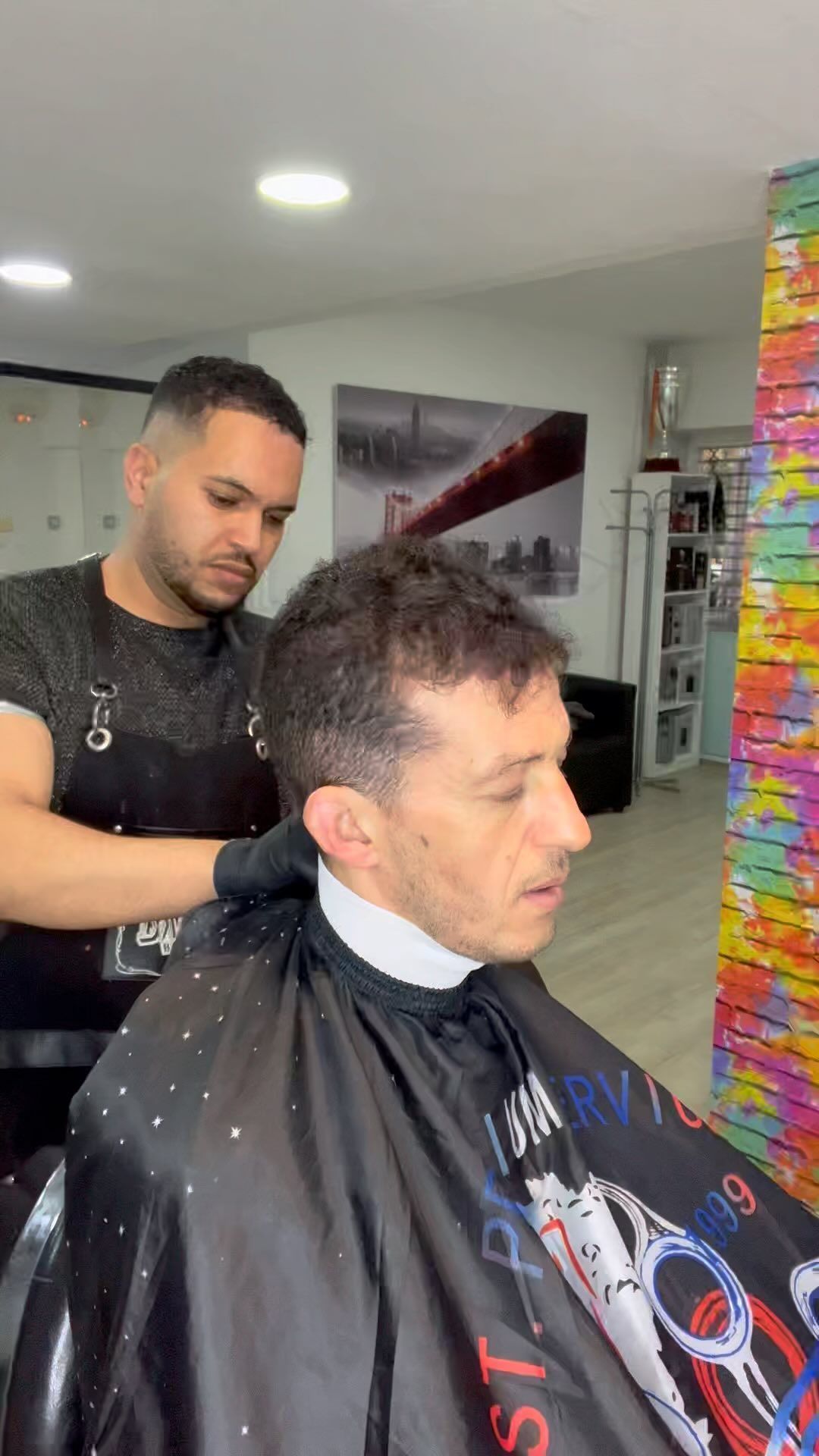 Un barbero corta el pelo a una clienta en un local decorado con mucho estilo. Lleva guantes negros y delantal.