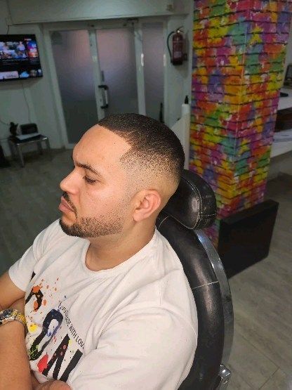 Hombre con corte de pelo descolorido en silla de barbero; fondo borroso del salón.