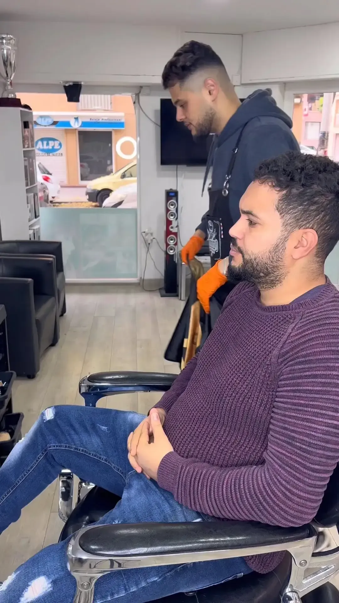 Un barbero corta el pelo a un cliente en un salón. El cliente está sentado en una silla.