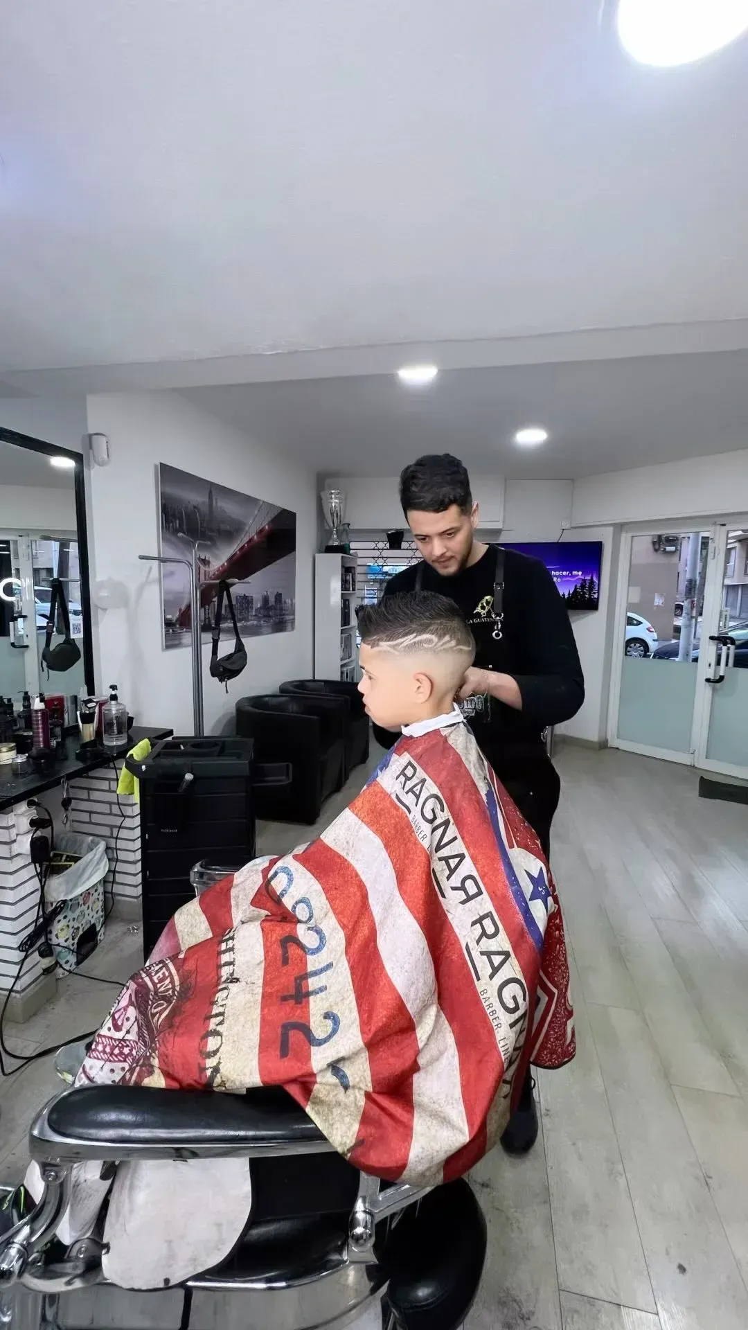 Un barbero corta el pelo a un joven en una barbería con una maquinilla. El joven lleva una capa a rayas.