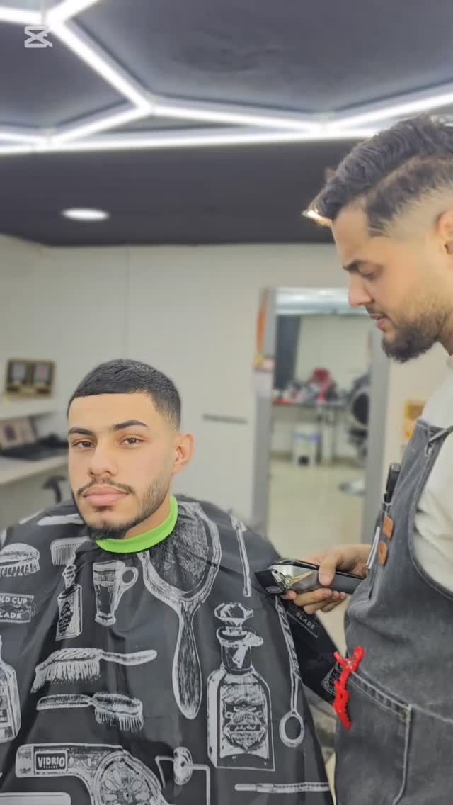 Un barbero le corta el pelo a un hombre en un salón muy iluminado.