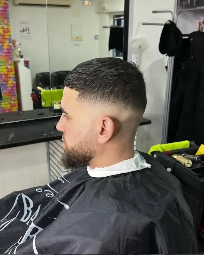 Hombre con un corte de pelo descolorido en una barbería, vistiendo una capa negra.