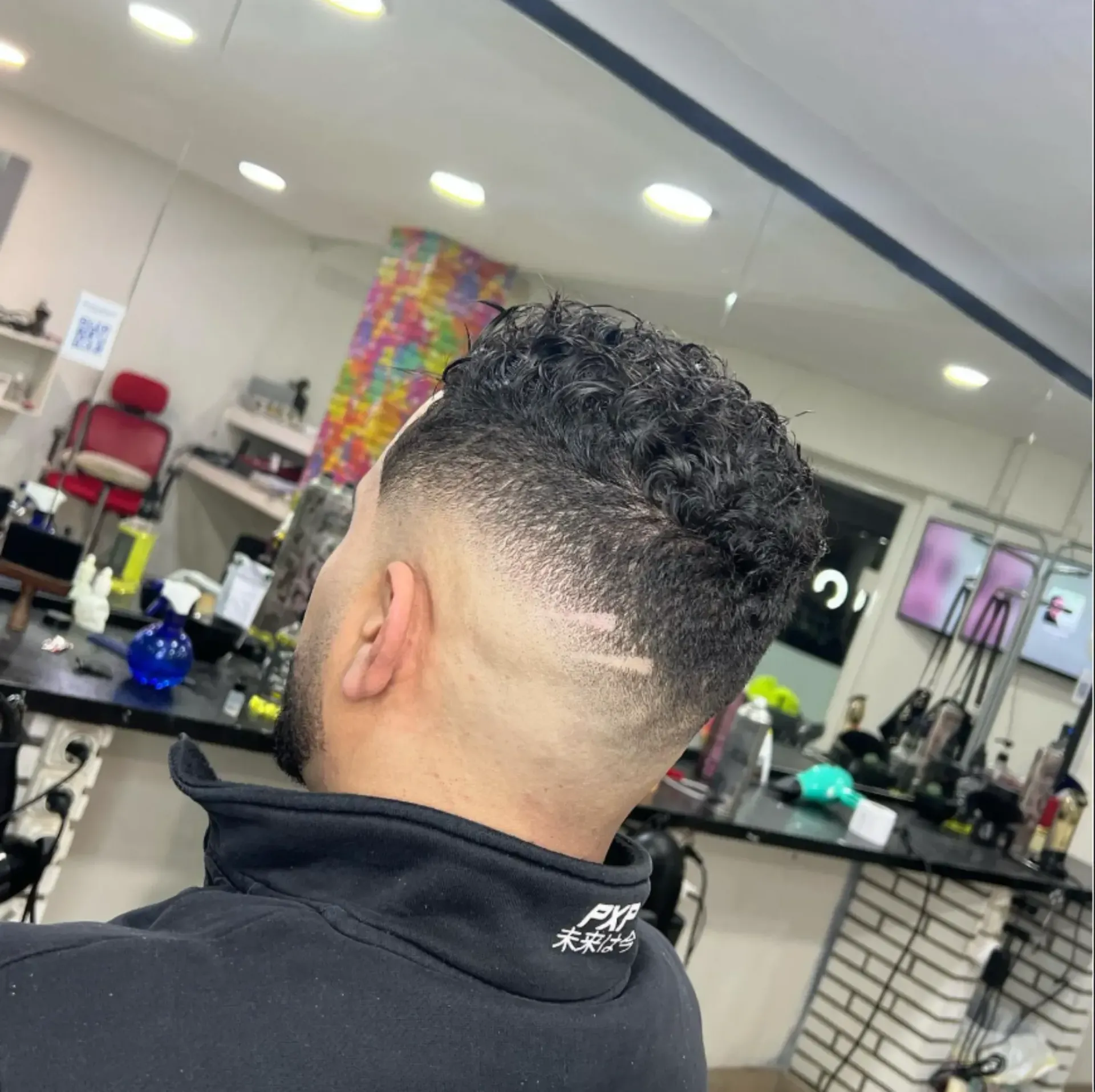 Hombre con cabello oscuro y texturizado y corte desvanecido, en una barbería.