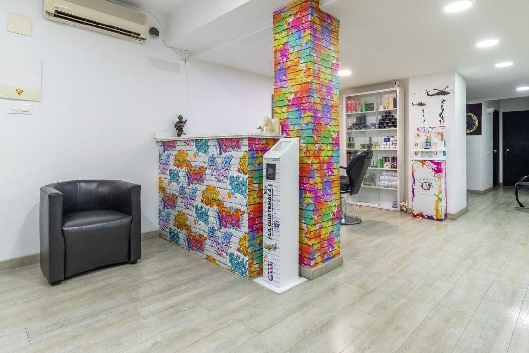 Interior de salón con una columna de ladrillos de colores y un mostrador de recepción. Silla negra, paredes blancas y suelo luminoso.