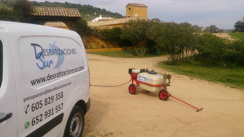 Una camioneta de trabajo blanca estacionada en un camino de tierra al lado de un pulverizador químico móvil que está siendo remolcado en un entorno rural al aire libre.