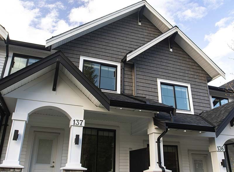 Una casa adosada de dos pisos con columnas blancas, una fachada superior de tejas grises y el número de casa 137 en el porche delantero.