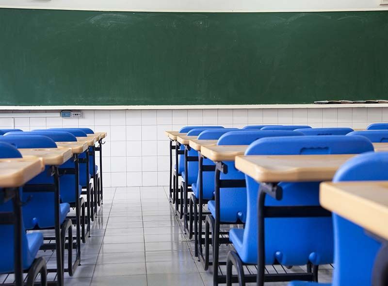 Aula vacía con filas de sillas azules frente a una pizarra verde y paredes de azulejos.