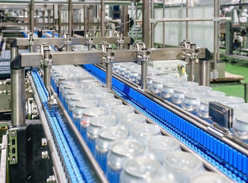 Las latas de bebidas plateadas se mueven a lo largo de una cinta transportadora industrial azul en una planta de fabricación.