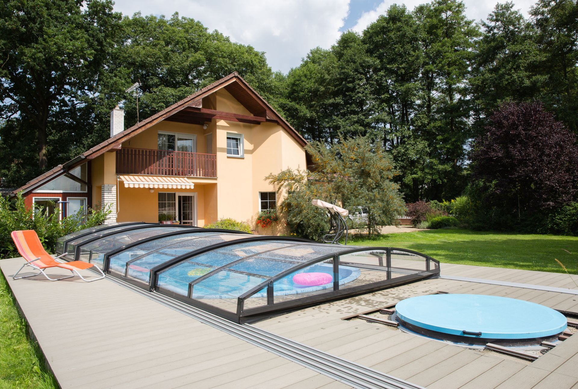 Vue sur une piscine couverte avec maison ayant des volets roulants en second plan
