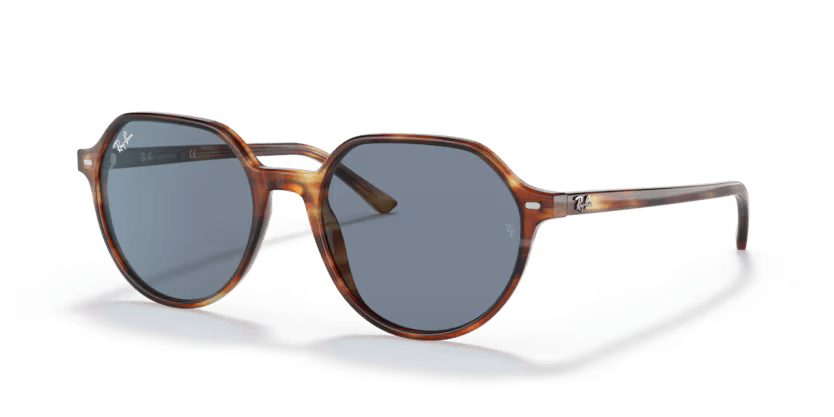 Un par de gafas de sol Ray-Ban están sobre una superficie blanca.