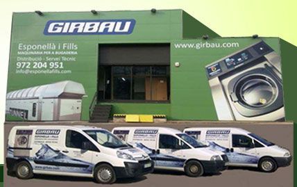 Un edifici verd amb rètols de Girbau i tres furgonetes de servei de la marca aparcades davant, que anuncien maquinària de bugaderia.