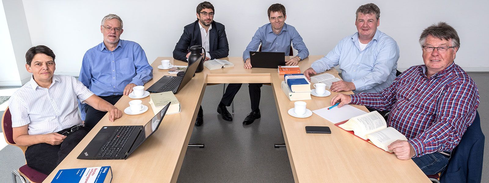 Eine Gruppe von Männern sitzt mit Laptops und Büchern um einen Tisch