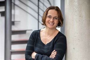 Eine Frau lehnt mit verschränkten Armen an einer Säule und lächelt.