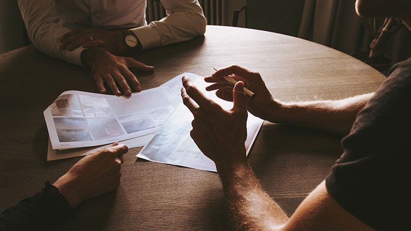 Zwei Männer sitzen mit Papieren in den Händen an einem Tisch.