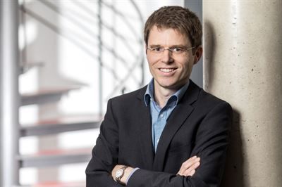 Ein Mann im Anzug lehnt mit verschränkten Armen an einer Säule.