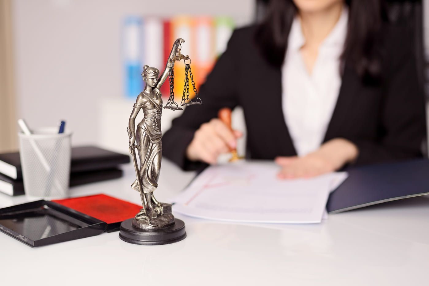Una mujer está sentada en un escritorio con una estatua de la justicia.