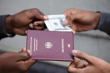 Un hombre le da a otro hombre un pasaporte y un billete de dólar.