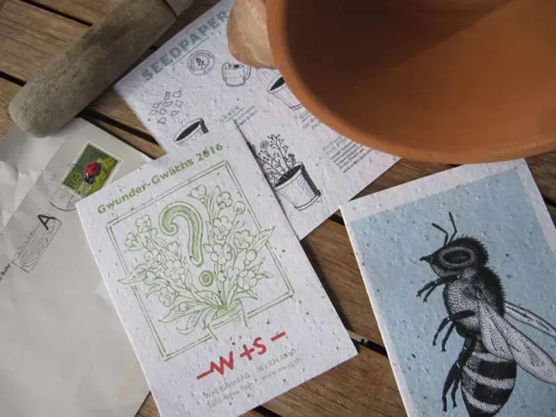 Schreibtisch mit Skizzenbuch, Buntstift, Terrakottatopf und einer Bienenzeichnung auf blauem Papier.