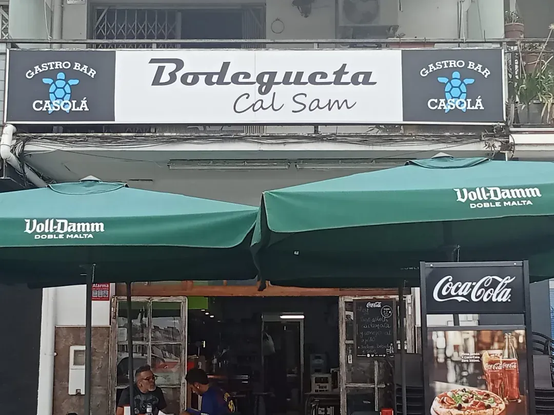 Bistro Bodegueta Cal Sam con sombrillas verdes y cartel de Coca-Cola.