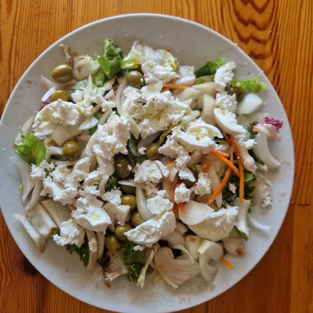 Ensalada con queso feta, aceitunas y cebollas en un plato blanco.