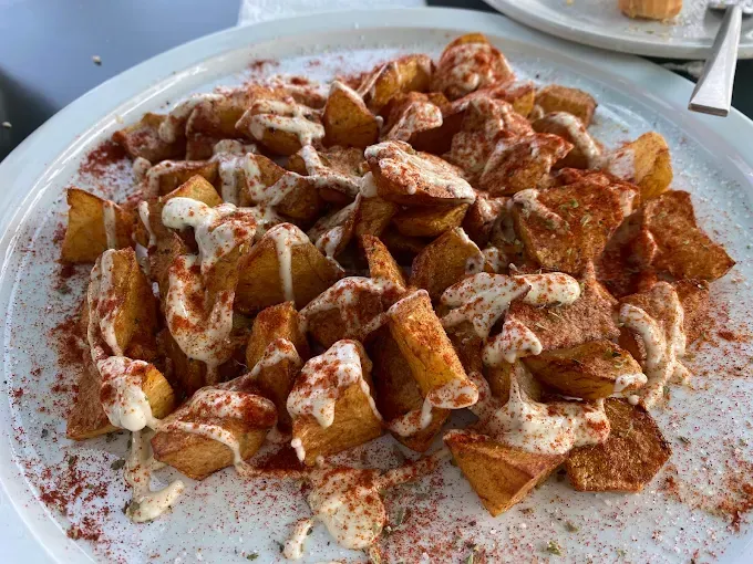Patatas gajo fritas con salsa cremosa y pimentón, en un plato blanco.
