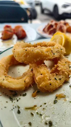 Anillos de calamares fritos en un plato con rodajas de limón y otros platos borrosos en el fondo.