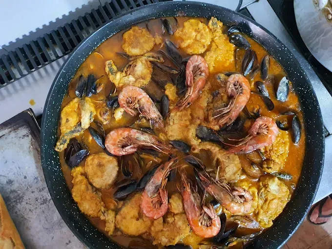 Paella de mariscos en una sartén grande, con camarones, mejillones y vieiras, con una salsa dorada.