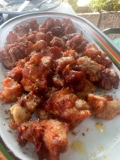 Trozos de panceta de cerdo fritos en un plato blanco, relucientes con aceite y condimentos.