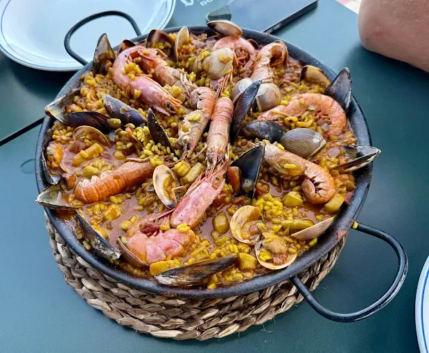 Paella de mariscos en una sartén grande sobre una estera tejida, con camarones, mejillones y almejas.