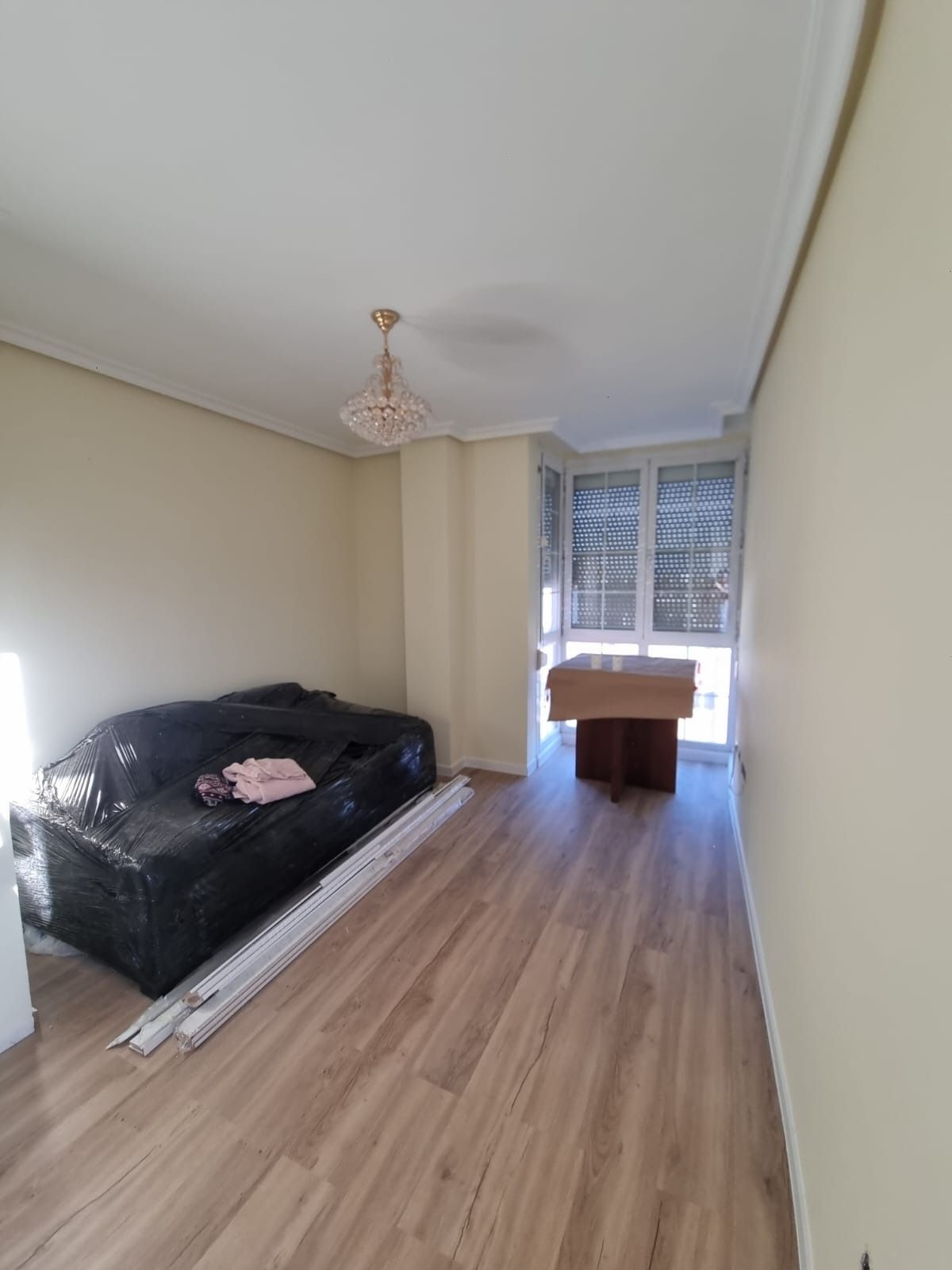 Habitación vacía con pisos de madera, sofá, mesa y una ventana con persianas.