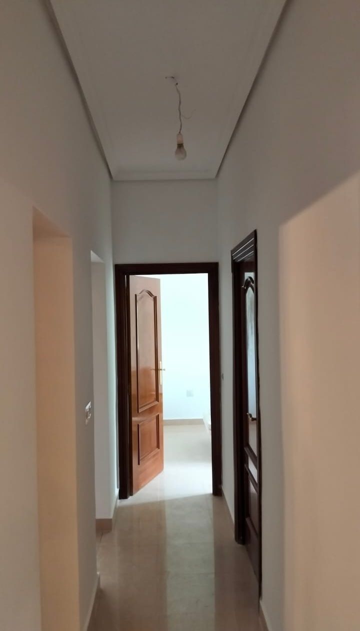 Pasillo con paredes blancas, puertas marrones y una única bombilla expuesta.