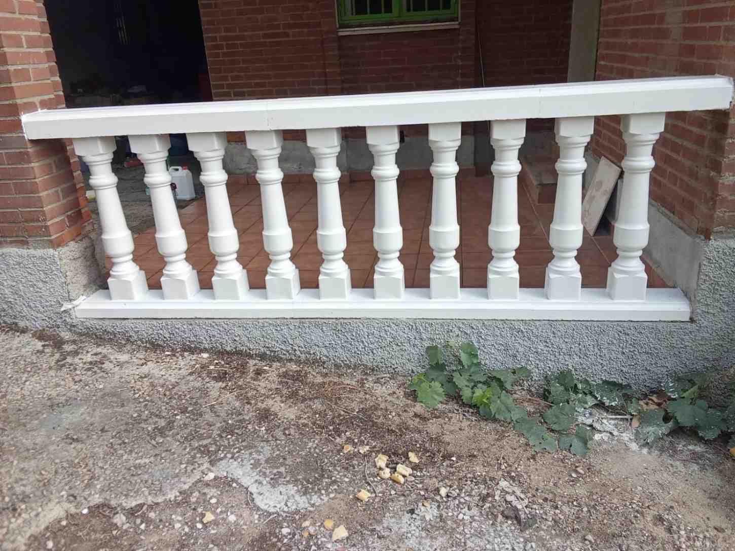 Barandilla blanca en el porche de un edificio de ladrillo, con base de grava y algunas plantas.