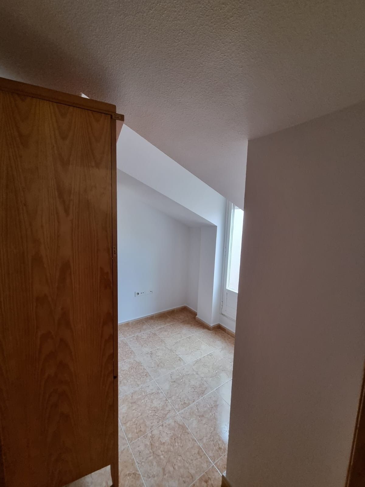 Armario de madera a la izquierda, puerta a una habitación con techo inclinado