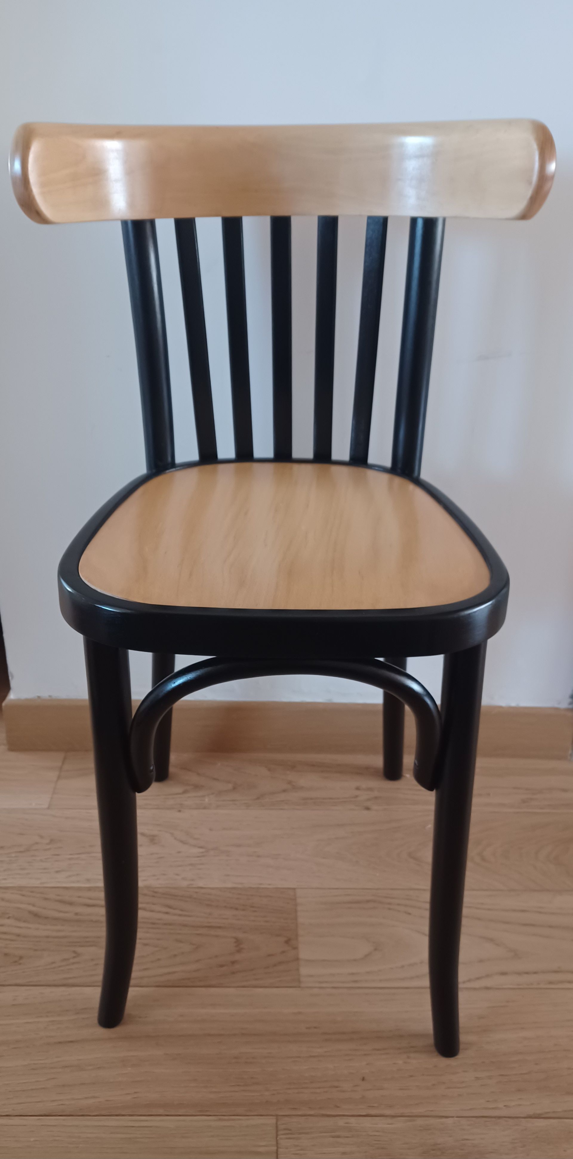 Chaise en bois noir avec assise et dossier en bois clair sur un parquet.