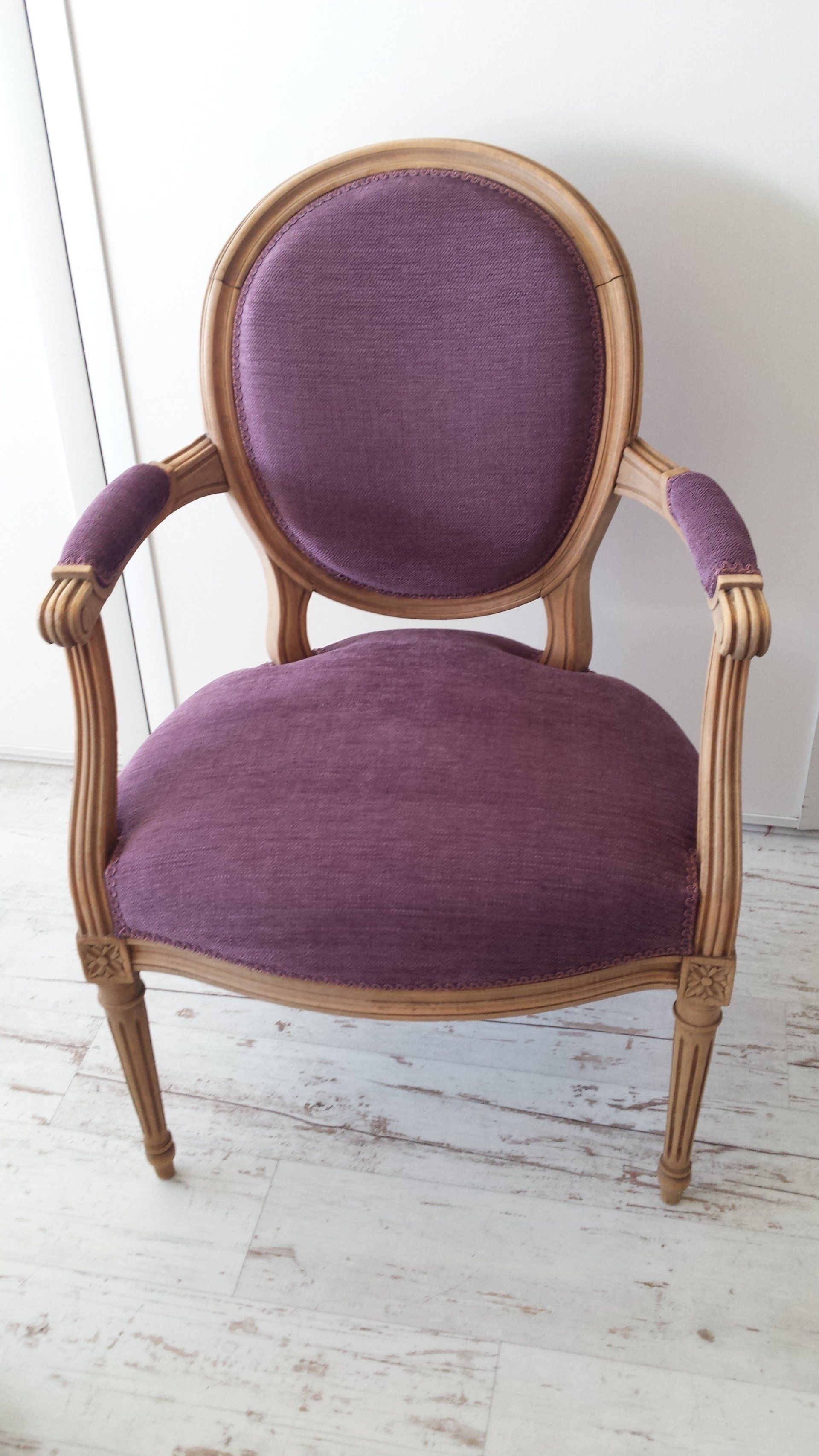 Fauteuil vintage violet capitonné avec structure en bois sur un sol blanc