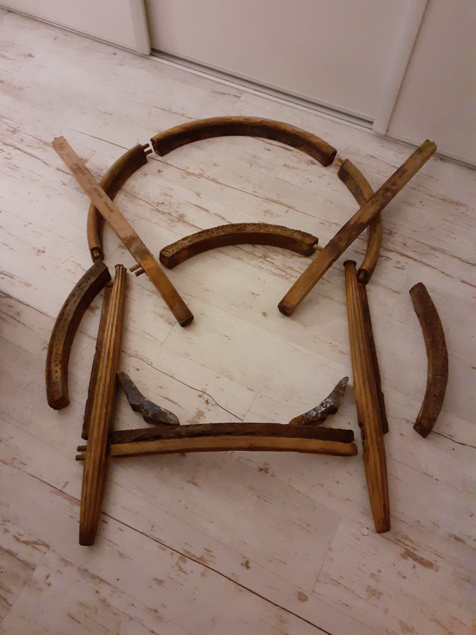Des morceaux de chaise en bois cassés sont éparpillés sur un sol carrelé clair, contre un mur.