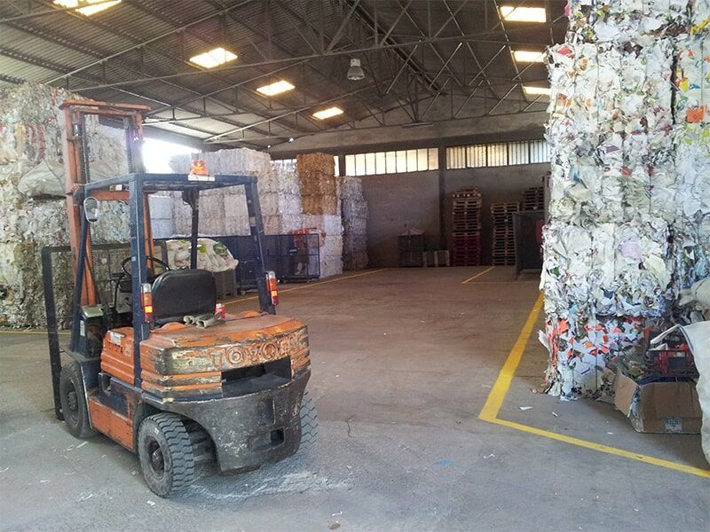 Empilhadeira em um armazém de reciclagem com pilhas de fardos de papel.
