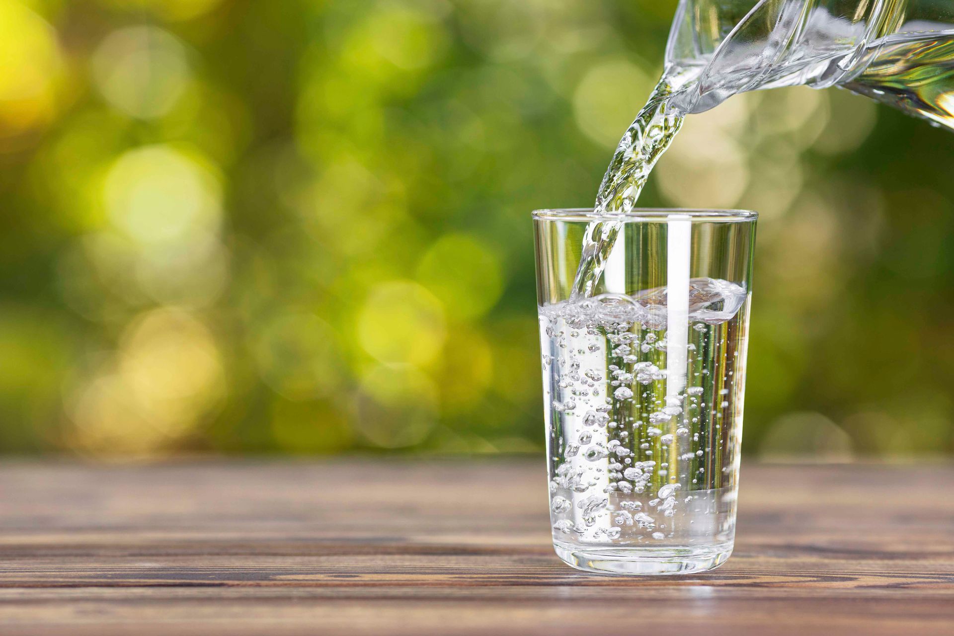 Auf einem Holztisch wird Wasser in ein Glas gegossen.