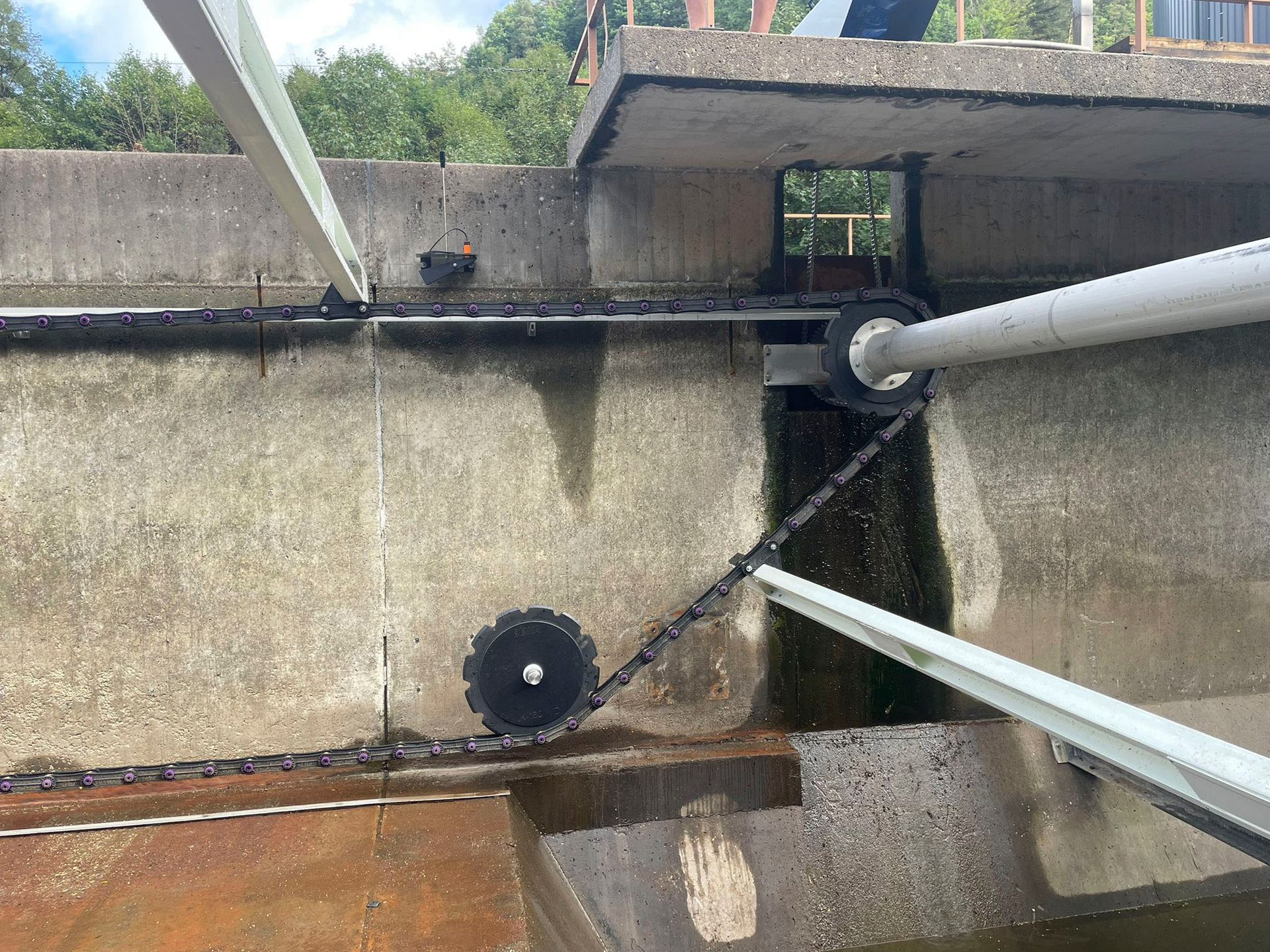 Eine Betonwand, durch die eine Kette verläuft und aus der ein Rohr herauskommt.